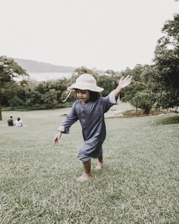 a little girl in a blue hat and blue dress is running in the grass at The parcHAUS at Firewheel Parkway