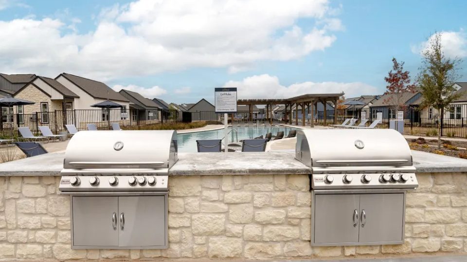 a large outdoor kitchen with two grills and a pool at The parcHAUS at Celina Parkway