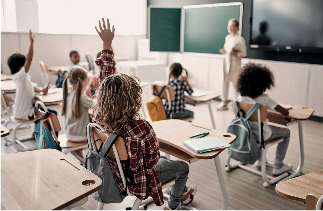 a classroom with children sitting at desks and raising their hands at The parcHAUS at Celina Parkway